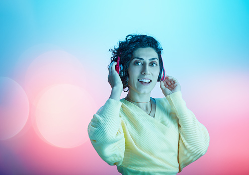 Beautiful young woman enjoying her favorite music against multicolored background