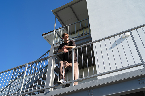 Low angle of young adult man standing beside apartment complex on his neigborhood