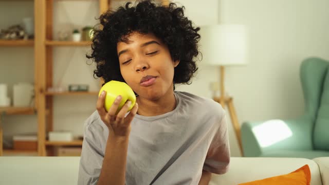 Happy pretty girl biting green apple at home. Beautiful african american young woman eating fresh fruit and smiling. Healthy food vegan vegetarian dieting concept. Healthy snack clean food.