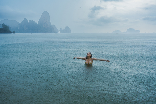 Young Caucasian woman swimming in the sea under the tropical rain