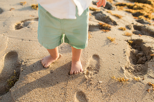 A 1-Year-Old Baby Boy Wearing a White Short Sleeve Button-Down Shirt & Blue Short, Barefoot on the Beach Enjoying & Discovering the Wonders of the Beach for the First Time During a Golden Sunrise on Palm Beach, Florida in the Spring of 2023