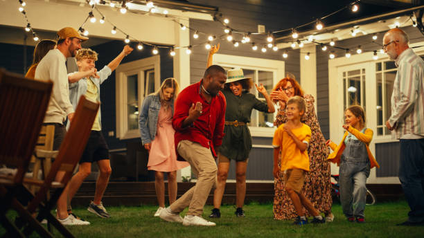 grupo de amigos y familiares multiculturales diversos divirtiéndose y bailando juntos en una fiesta nocturna en el jardín. hermosos y guapos jóvenes y viejos divirtiéndose. - cámara lenta fotografías e imágenes de stock