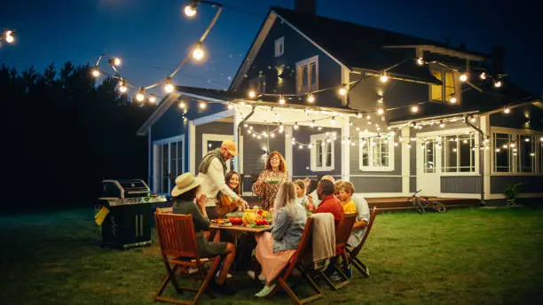 Group of Multiethnic Diverse People Having Fun, Sharing Stories with Each Other and Eating at Outdoors Dinner Party. Family and Friends Gathered Outside Their Home on a Warm Summer Evening.