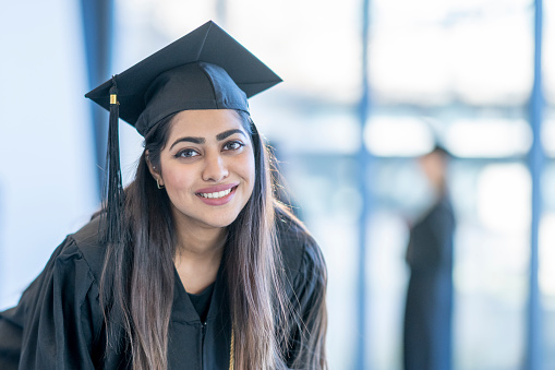 A class of 2024 charm on a yellow tassel on black graduation cap with a rolled diploma.