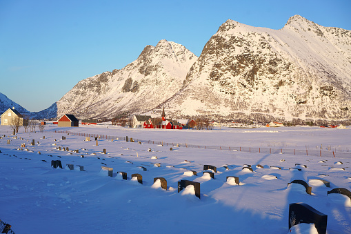With snow covered graveyard and red wooden church in background on Flakstadøya island, Lofoten, Nordland, Norway