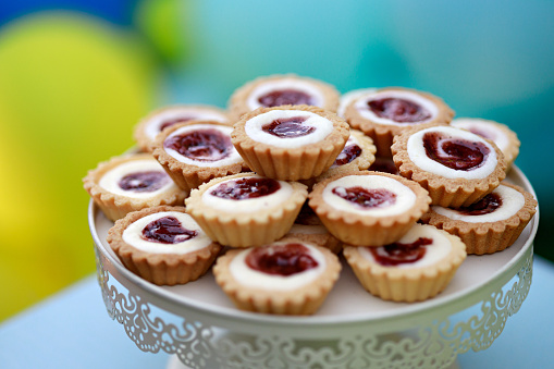 Mini raspberry tartlets are displayed on a pastry stand at a birthday party.