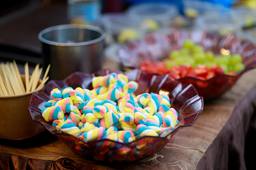 A bowl of colorful marshmallow candy is piled high on a buffet table.