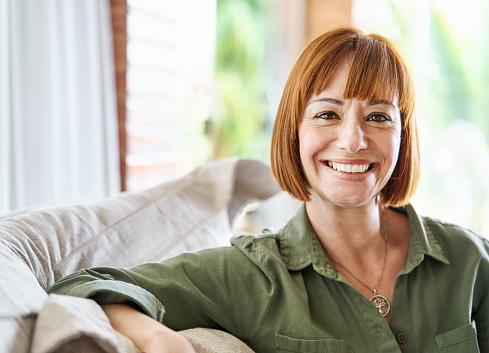 Portrait of a mature redheaded woman smiling while sitting alone on her living room sofa at home