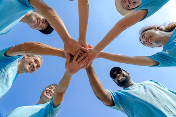 Group of happy diverse volunteers joining stacked hands together Group of happy diverse volunteers joining stacked hands together with smiles to show the power of unity in social environment charity working team, key success in making future a better world community outreach stock pictures, royalty-free photos & images