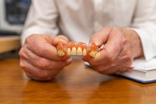 Dentures in the hands of a man in a white coat. Close up.