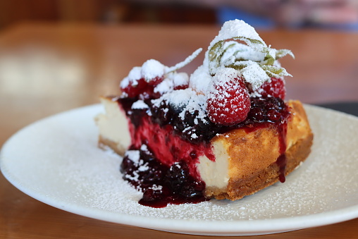 A slice of a summer fruit cheesecake on a white plate on a table in close up