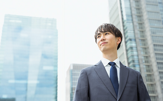 A man in a suit in his 20s and 30s looking far away with a serious expression in a business district