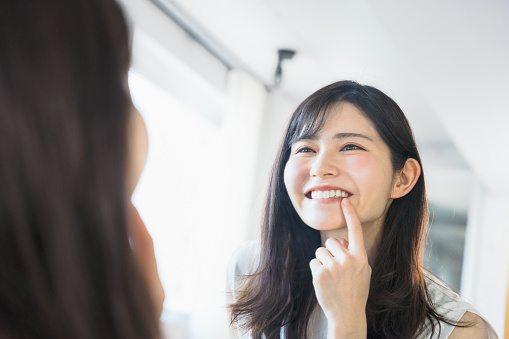 A woman in her thirties (beauty image) who looks at her face reflected in the mirror and makes her happy with the beauty and whiteness of her teeth (beauty image)