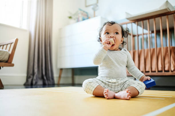 Child development, toys and a baby sitting on the floor in it's bedroom at home while playing or looking curious. Children, learning and growth with an adorable little girl kid in a house to play stock photo