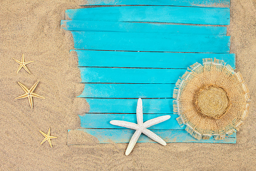 White and orange starfish with straw hat on blue rustic nautical wooden pier boards. Summer, sea background. Concept of travel, vacation. Copy space