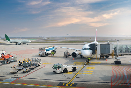 A plane boarding passengers on it’s stand with planes taxiing and taking off behind