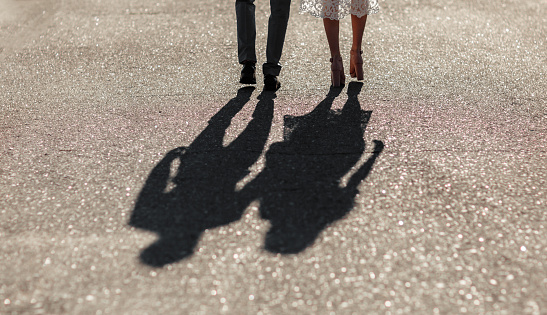Shadows of a young couple walking down the street holding hands. Bright sunny day. Newlyweds go far away in sun lights. Tenderness, love and relationship