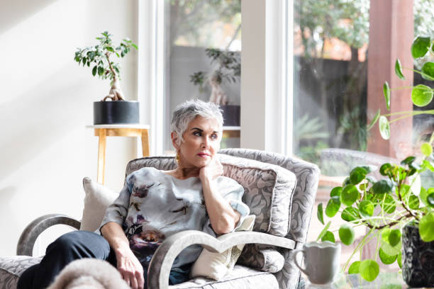 Sitting in her sunroom looking out the window, the senior adult woman becomes upset by her thoughts.