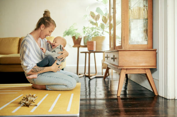 Mother smile, baby and play in home living room, bonding and having fun together. Development, happiness and mama holding child, kid or newborn, playing and care while enjoying quality time in house. stock photo