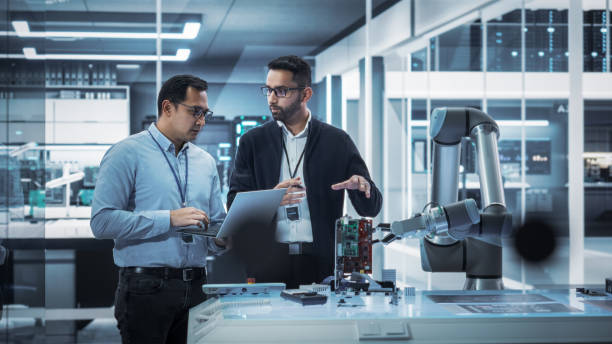 istock Diverse Colleagues of Industrial Robotics Engineers Experimenting With Robotic Arm. Scientists Use Laptop Computer to Manipulate and Program the Robot to Move and Put Down a Powerful Microchip. 1481700990