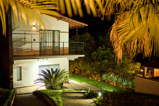 Exterior of a luxury two-story home and its grounds illuminated in the evening by brigth floodlights