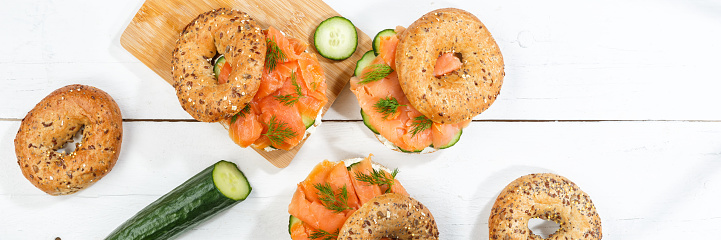 Bagel sandwich with salmon fish and cream cheese for breakfast panorama on a wooden board from above