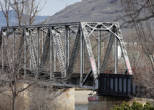 Kamloops, Canada - March 31, 2023: Two Canada Geese stand by the South Thompson Kamloops CNR Bridge. This railway bridge spans the South Thompson River from the north end of downtown Kamloops. Cloudy morning in the Thompson-Nicola Regional District.