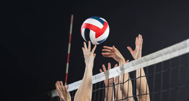 Female Volleyball Players In Action Female playing volleyball on net and jumping to hit ball during sports match. Team sport and healthy lifestyle concept. volleyball ball stock pictures, royalty-free photos & images