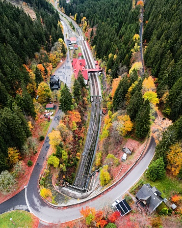 An aerial view of a winding rural road and train tracks, running through a dense forest in autumn