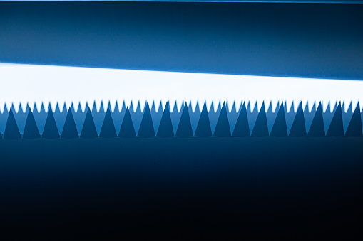 White sharp triangles protrude from the white body on a dark blue background, similar to shark teeth, another row of teeth in blur in the background.