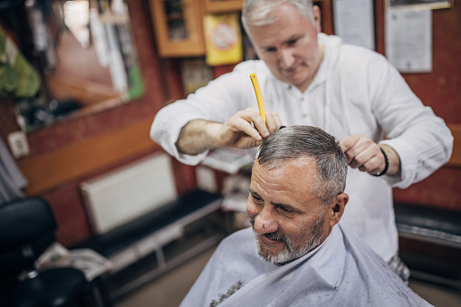 A hairdresser arranges the hair on the head of an elderly man
