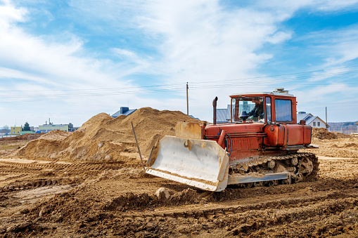 An old orange bulldozer performs work to level the sandy soil.