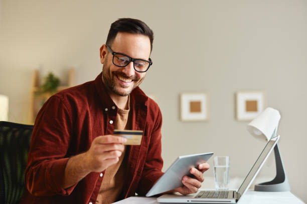 istock Young man holding credit card and tablet at home at table 1481717963