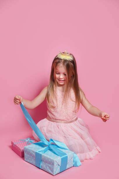 istock Cute excited kid girl opening present box sitting on pink studio background 1481719232
