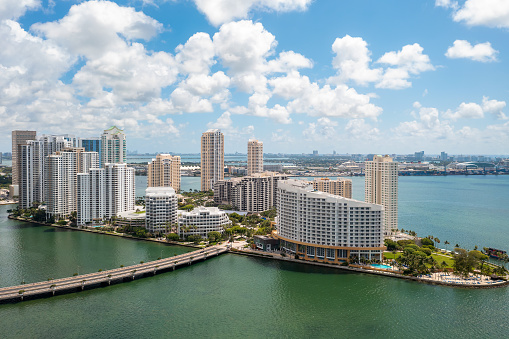 Aerial shot from a drone of the Brickell Key area, with a lot of towers and modern buildings, commercial urban landscape, surrounded by sea and canals, boats sailing, piers, bridges, avenues, blue sky and turquoise sea
