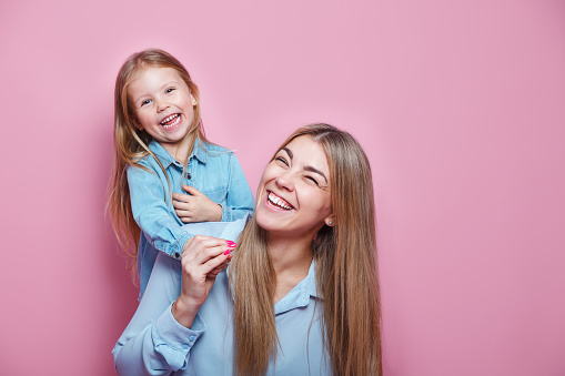 Happy family. Little girl hugs her mom and laughs on pink background