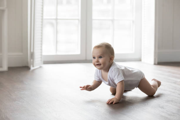 Happy baby in bodysuit crawling on knees stock photo