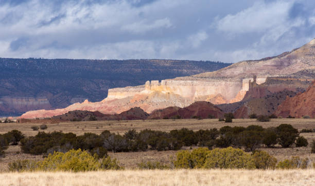 sonne beleuchtet bunte tafelberge und buttes mit bedrohlichem, dunklem himmel. nördliches new mexico. - great red spot stock-fotos und bilder