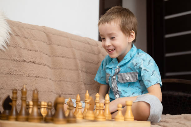 istock Cute little caucasian boy playing chess at home. Young boy intensely develops chess strategy playing board games with friends, sister, brother. Early development and additional education. 1481732484