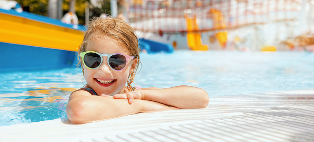 happy little girl with sunglasses in swimming pool at outdoor water park on sunny summer day. banner with copy space