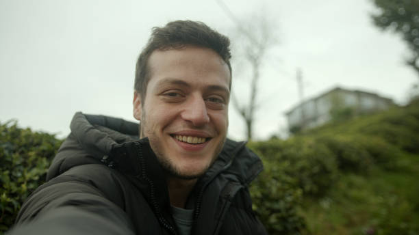 istock Young Brown-Haired Man in a Black Jacket Conducts a Video Conference Against a Beautiful Nature House Background - POV Shot 1481739253
