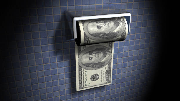 A toilet is filled with money, including hundred dollar bills. More money is scattered on the floor. A concept of throwing money down the toilet, a phrase meaning to waste money.