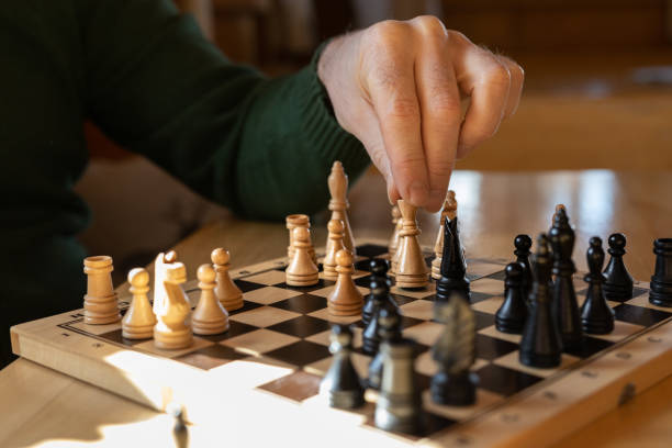 istock A man sits at a wooden table and makes a chess move with a white piece. 1481743332