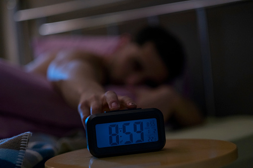 Man turns off alarm clock in bed