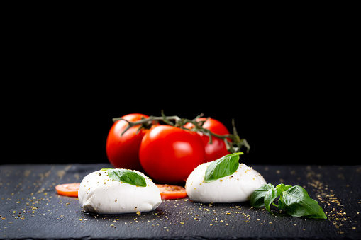 Caprese salad ingredients in closeup. On tray, there is mozzarella cheese, tomatoes und basil