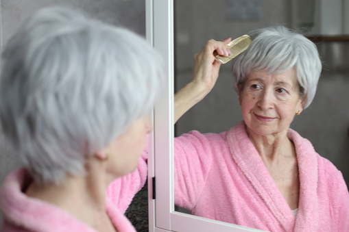 A very cute senior woman in her sixties is combing her hair. She looks satisfied with her natural hairstyle.