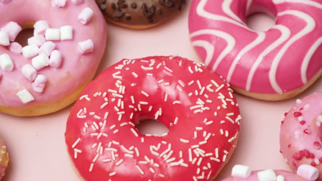 Donuts with red, pink and chocolate icing and marshmallows spin the view from above