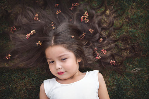 Little girl in white dress lying on the grass, she is smiling and her hair is very long and princess-like, children's day theme.