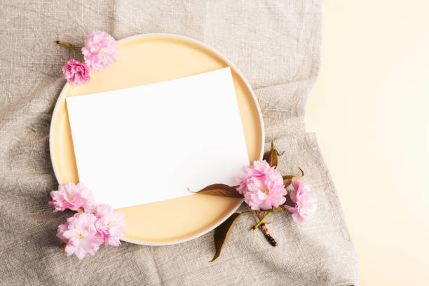 istock Plate with blank card and cherry blossom on beige fabric. Top view, flat lay, mockup 1481755799