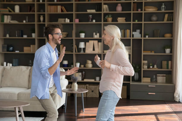 Cheerful retired mom and active adult son guy enjoying movement Cheerful energetic old retired mom and active adult son guy enjoying movement, fitness activity at home, dancing to music together in modern living room, smiling, laughing teacher retirement party stock pictures, royalty-free photos & images
